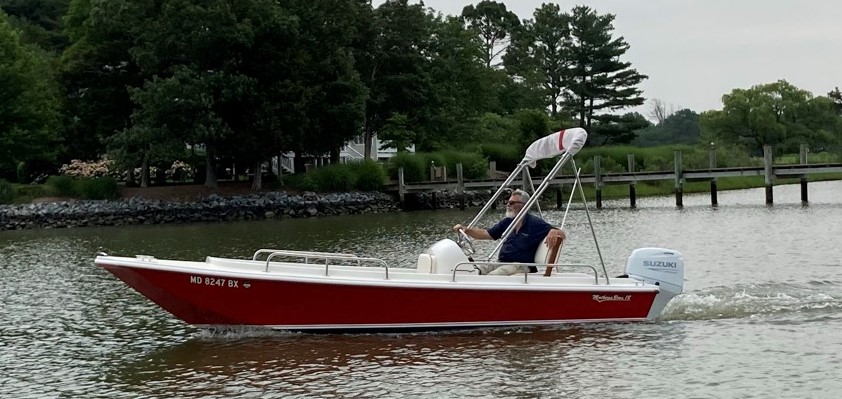Silver-haired man wearing shades and a blue shirt driving a red boat